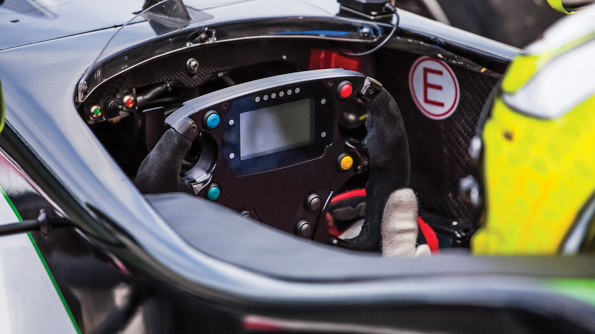 Close-up of a racing car cockpit showing the steering wheel with digital display and control buttons.